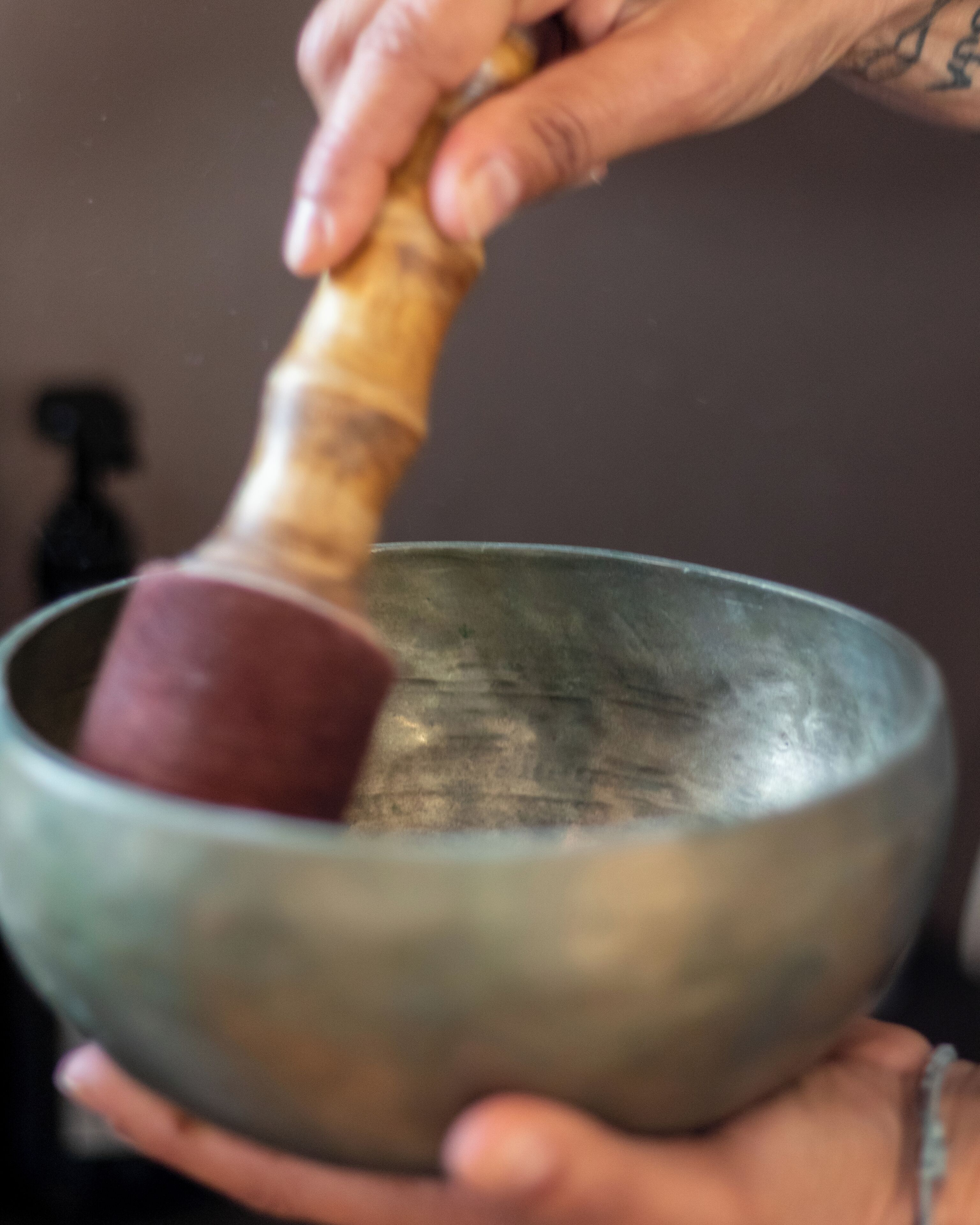 A person holding a metallic bowl with a wooden mallet.