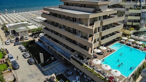 Un hotel de varios pisos con piscina en la azotea, asientos al aire libre y vistas al mar.