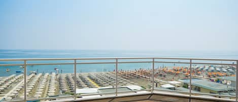 A wooden deck with a view of a beach area featuring rows of umbrellas and sun loungers.