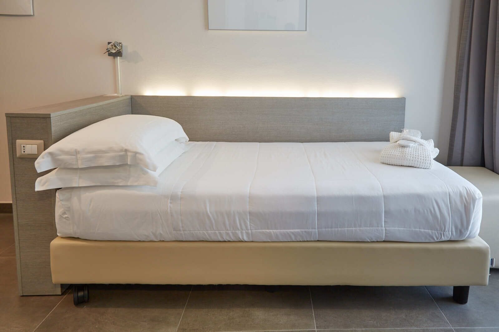 Una habitación de hotel moderna con una cama grande, una mesita de noche y una lámpara de pared.