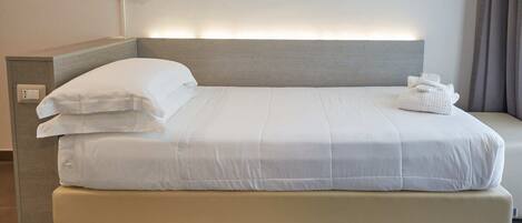 A modern hotel room with a large bed, a bedside table, and a wall-mounted light.