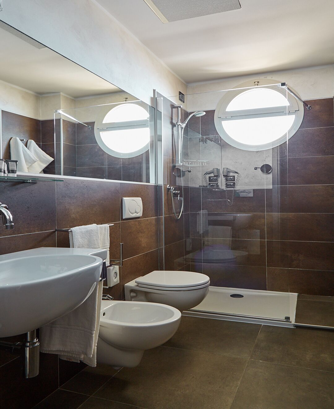 Un baño moderno con ducha envuelta en vidrio, dos inodoros, un bidé y un lavamanos grande.