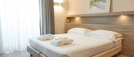 A hotel room with a bed, white linens, a headboard, and a wall-mounted light fixture.