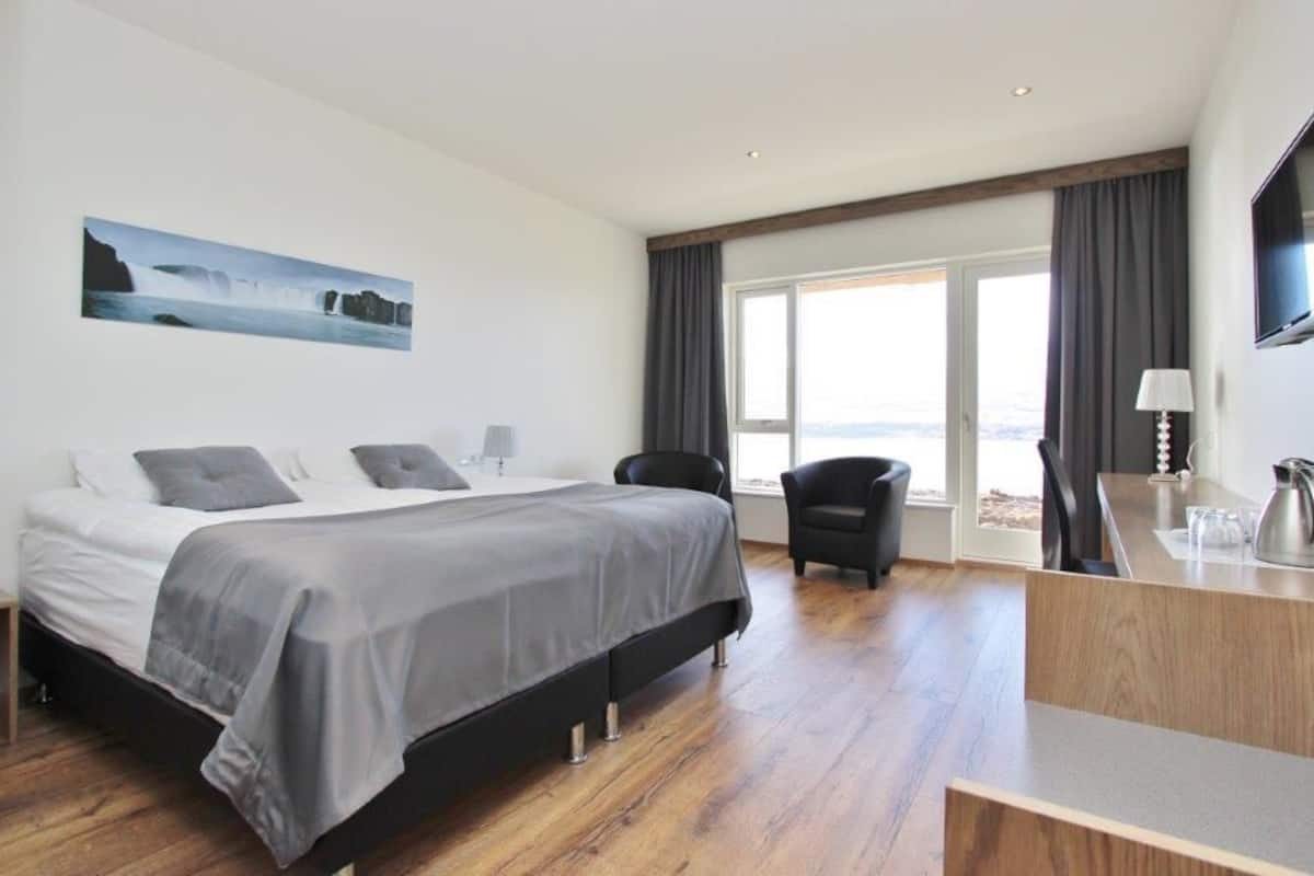 A modern hotel room with a large bed, a desk, a chair, and a TV.