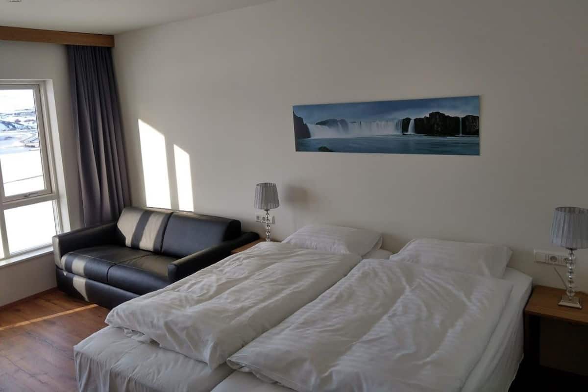 A hotel room with a bed, a sofa, a painting of a waterfall, and a window with curtains.