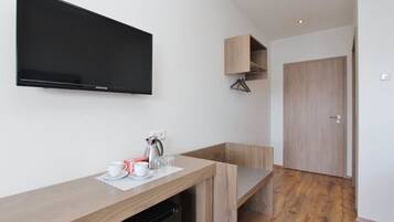 Ein modernes Zimmer mit einem wandmontierten Flachbildfernseher, einer Holzauskładung mit Kaffeezubehör und einer Holztür.