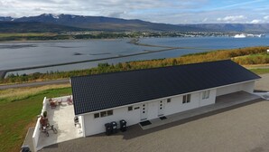A building with a flat roof, a gravel driveway, and a view of a lake and mountains in the background. - Hafdals Hotel (Akureyri)
