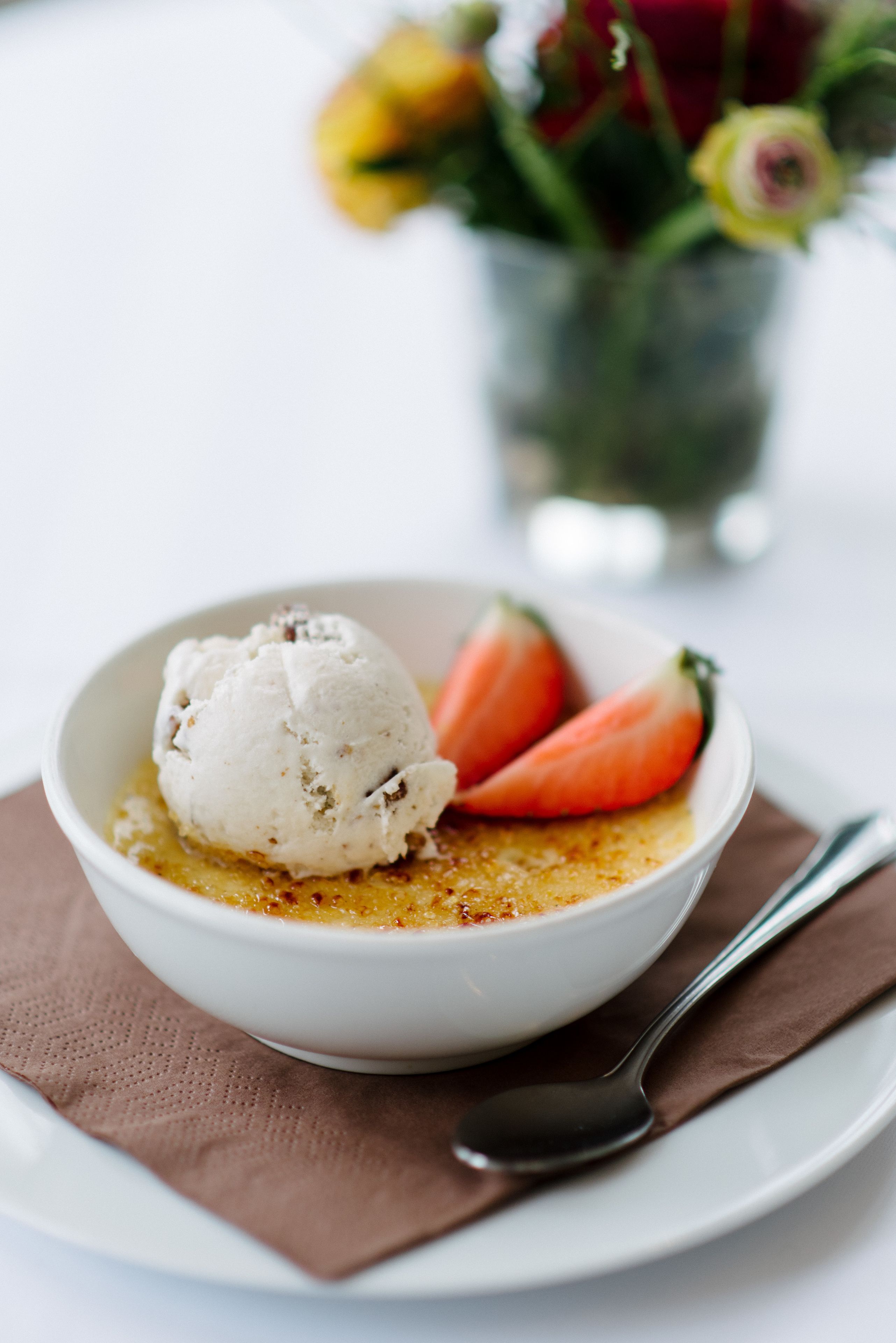 A dessert bowl with ice cream and strawberries on a white plate.