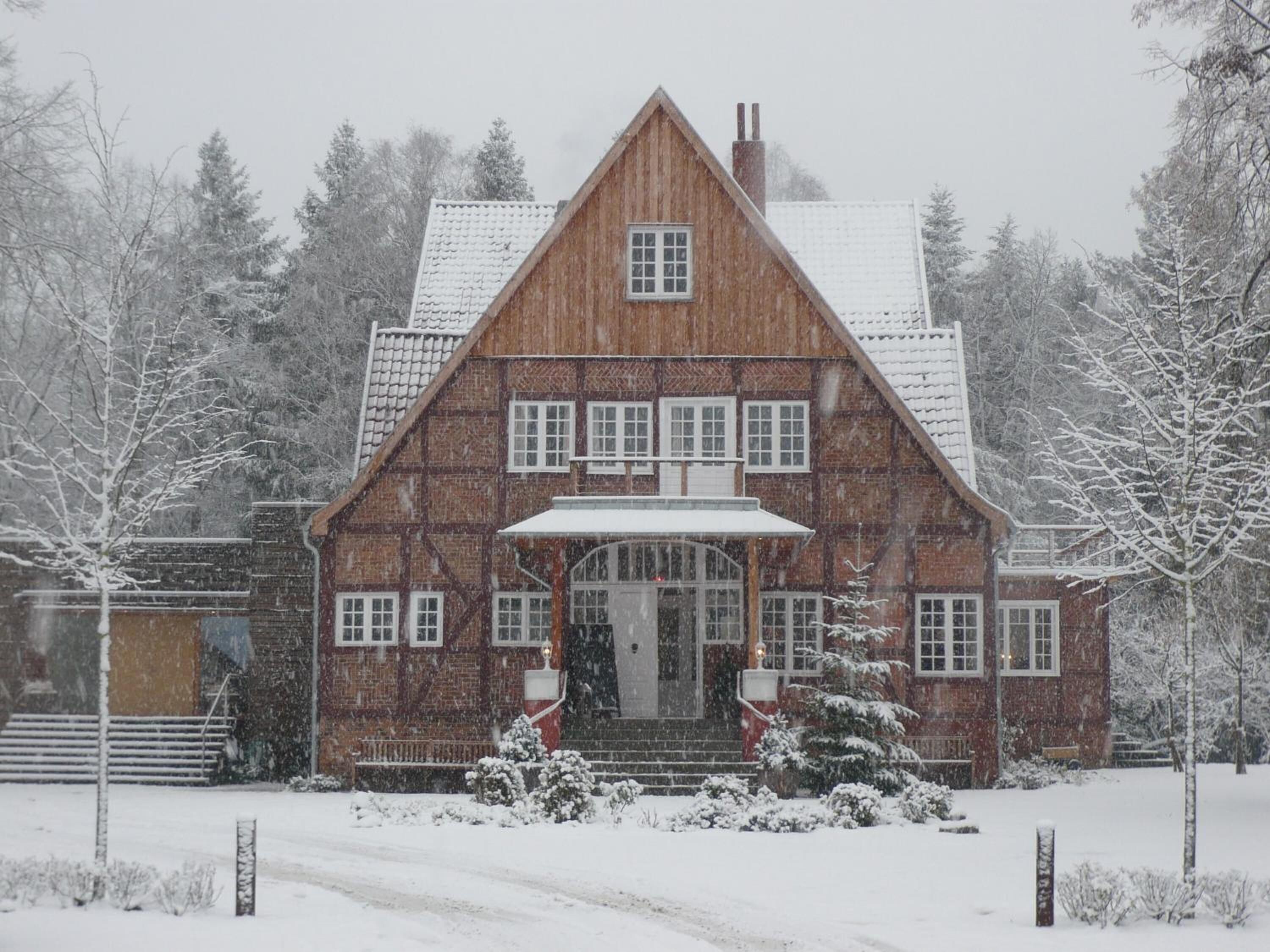 A two-story wooden house with a steeply pitched roof, multiple windows, and a central entrance with steps.
