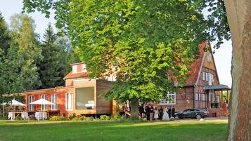 A traditional building with a large tree in front, surrounded by a grassy area and other trees.