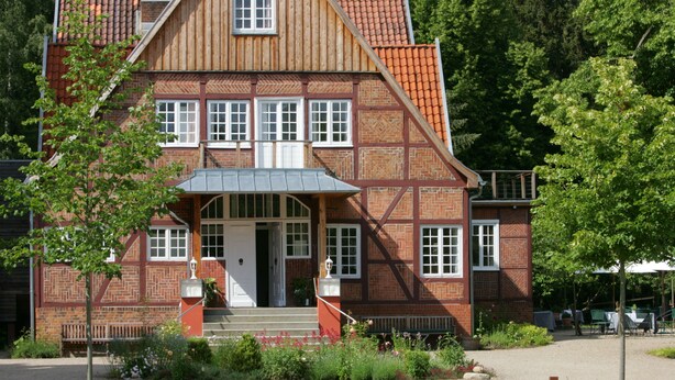 A traditional half-timbered building with a symmetrical facade, a central entrance with steps, and a small porch area.