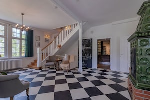 A hotel lobby with a checkered floor, a staircase, a chandelier, and a green decorative piece.