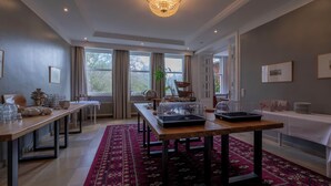 A spacious room with a long wooden table, a red patterned rug, and a chandelier.