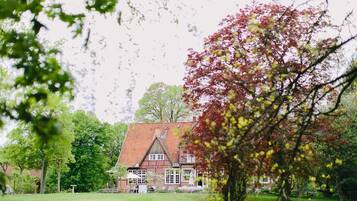 Une maison traditionnelle avec un toit recouvert de tuiles rouges, entourée d’une pelouse bien entretenue et d’arbres.