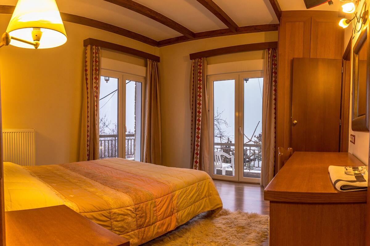 A hotel room with a bed, a wooden desk, a fluffy rug, and a balcony with a view.