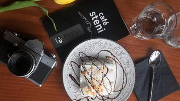 Ein Desserteller mit Schlagsahne und Schokoladenglasur, eine Vintage-Kamera, eine Speisekarte und ein Glas Wasser auf einem Holztisch.