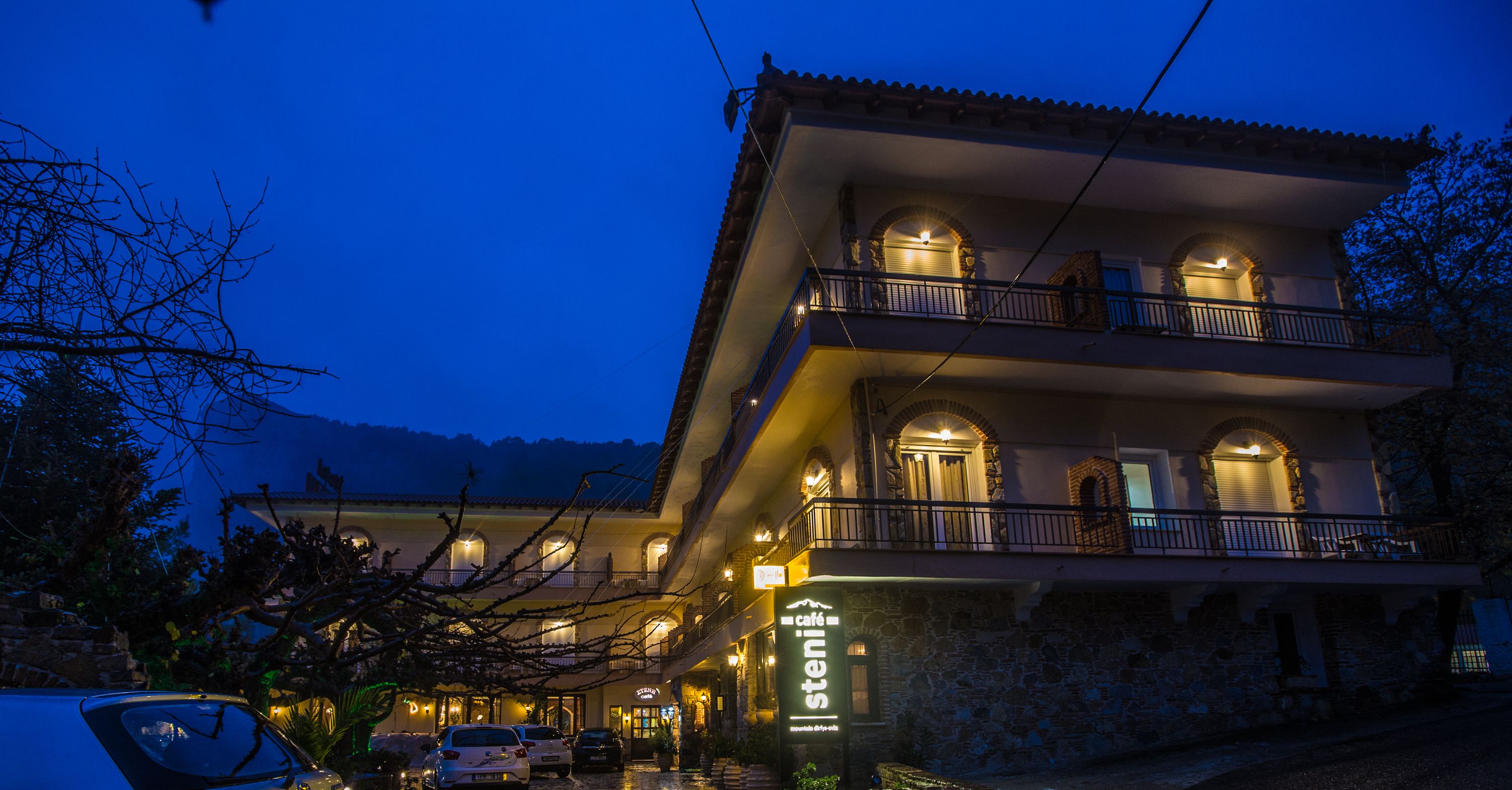 Un edificio de varios pisos con una cafetería en la planta baja, balcones y fachada de piedra.