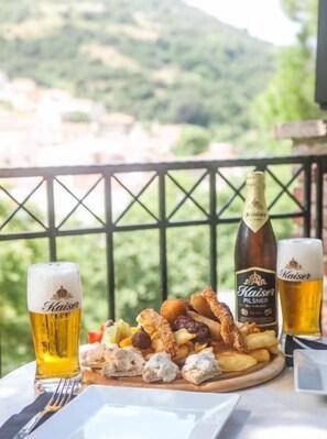 Une table avec une assiette de nourriture, deux verres de bière et une bouteille de bière, le tout sur un balcon offrant une vue panoramique.