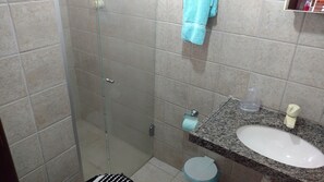 Un baño con cabina de ducha de vidrio, encimera de granito con lavamanos y un inodoro.