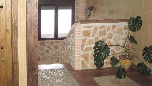 A stone-walled room with a wooden door, a window, and a potted plant. - Posada de los Consules Consuegra (Consuegra)