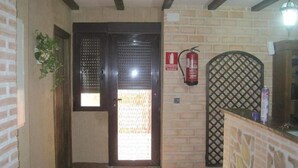A hallway with a wooden door, a fire extinguisher, and a tiled floor. - Posada de los Consules Consuegra (Consuegra)