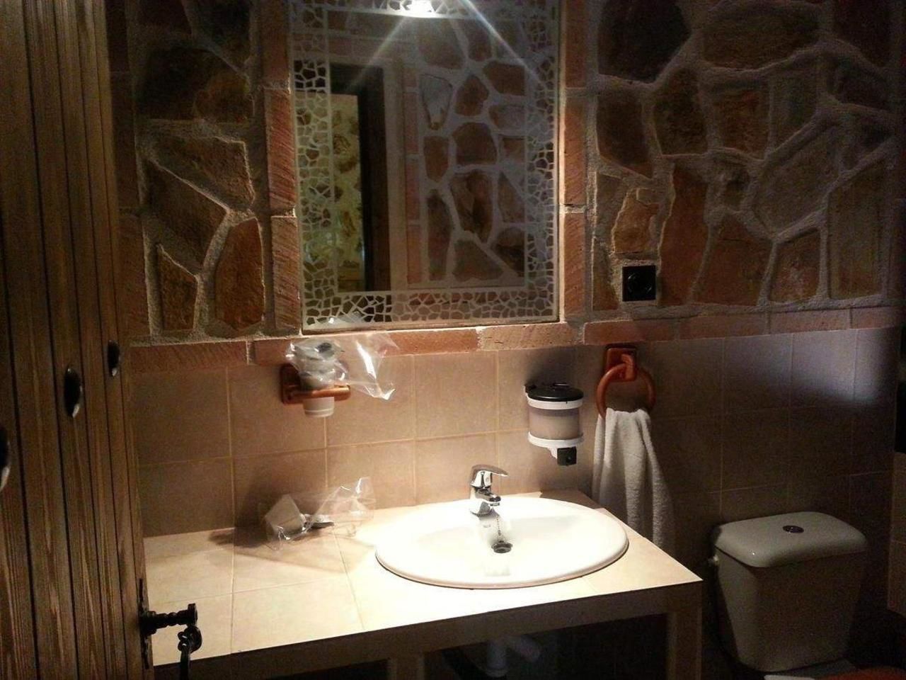 A bathroom with a stone wall, a sink, a mirror, and a toilet.