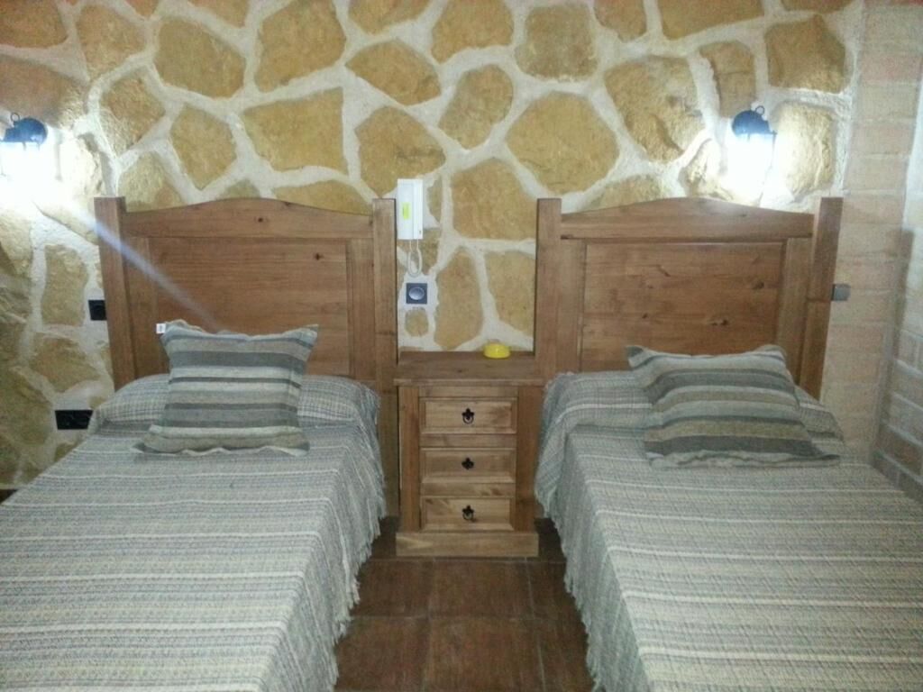 A room with two beds, a stone wall, and a wooden dresser with drawers.