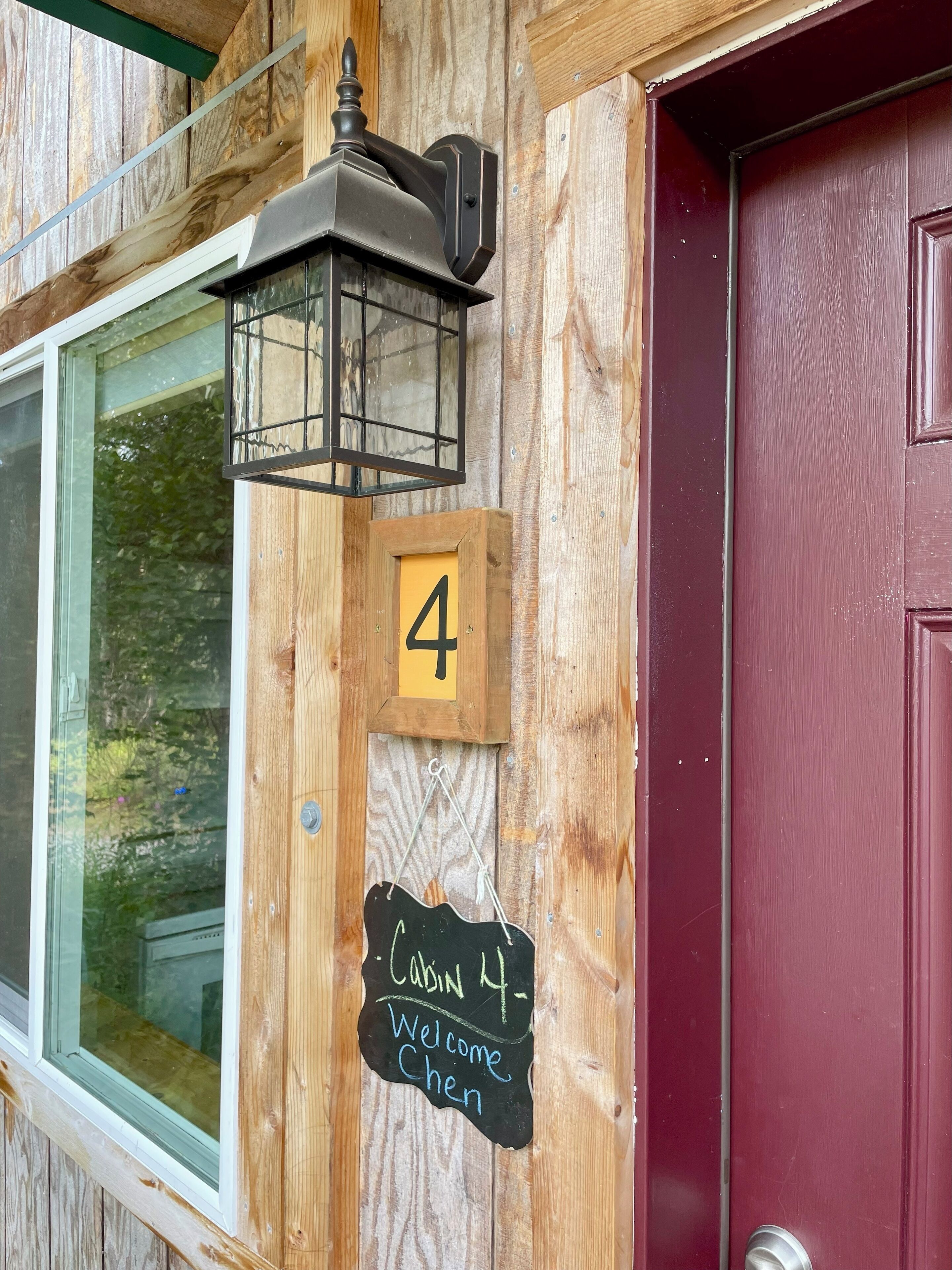 A wooden cabin with a black lantern, a number 4 sign, and a chalkboard sign reading "Cabin 4 Welcome Chen".