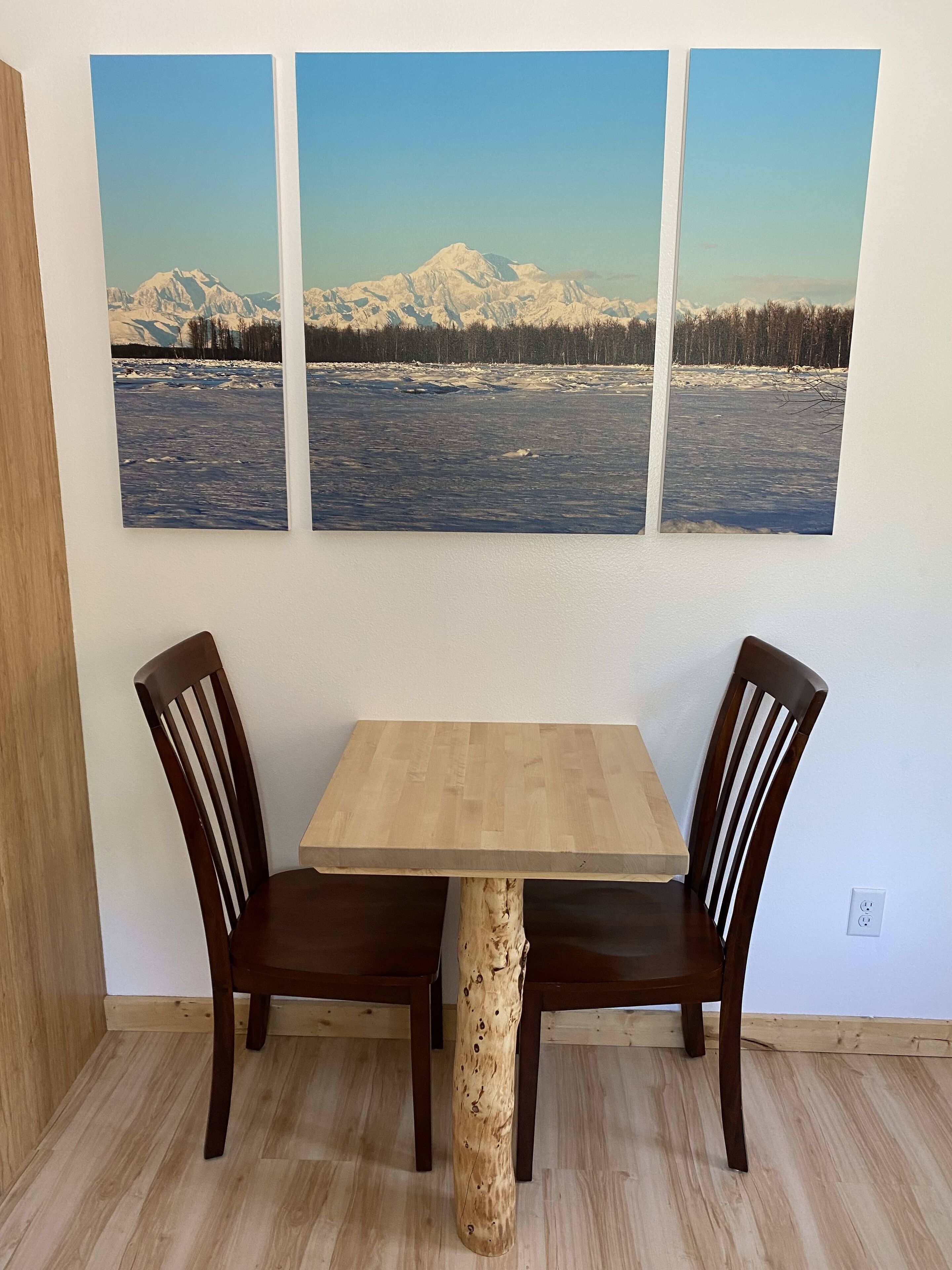 A dining table with two chairs, a wooden table base, and a wall-mounted picture of a snowy mountain landscape.
