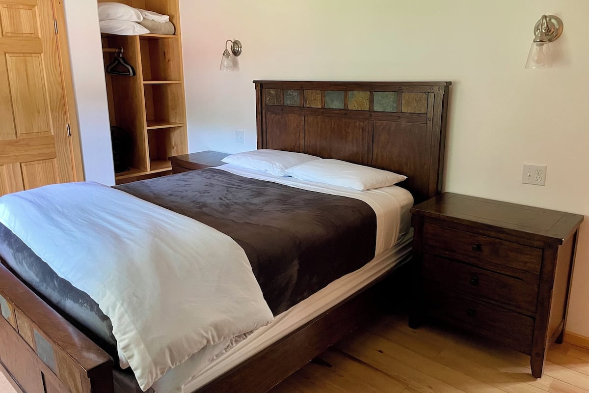 A bedroom with a wooden bed, a nightstand, a wooden wardrobe, and a wall-mounted light fixture.