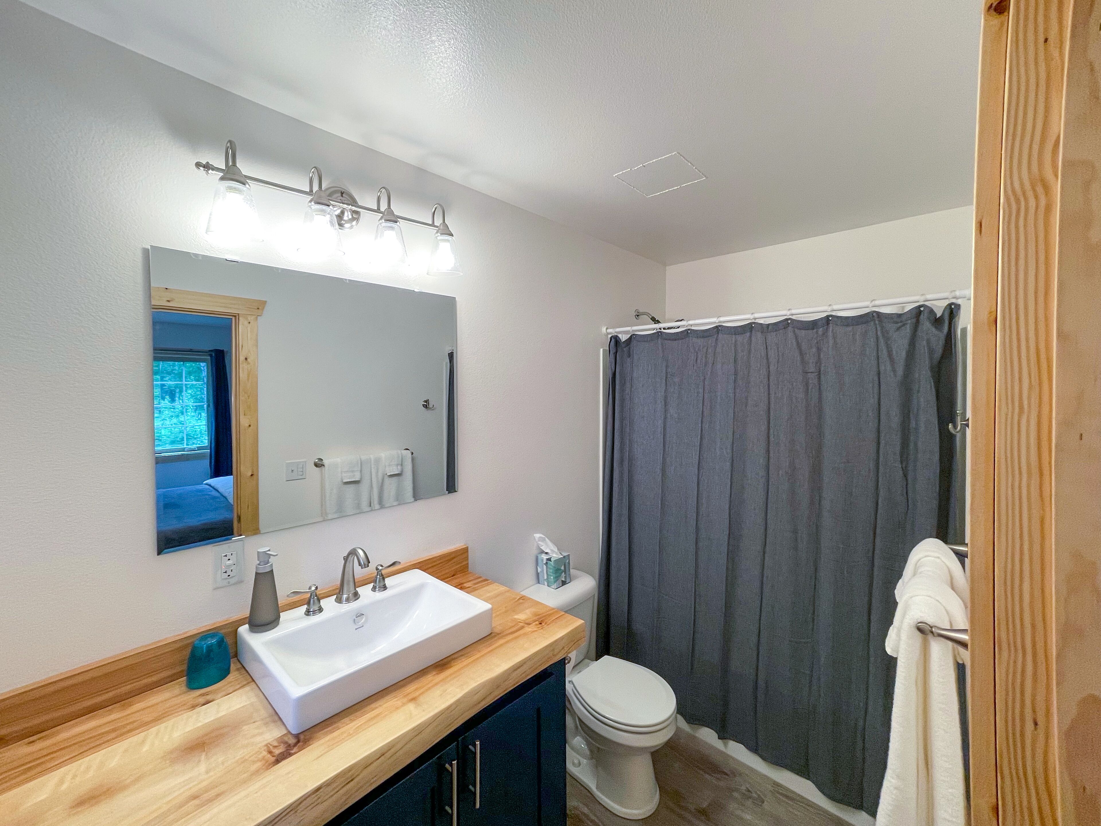 A bathroom with a wooden vanity, a white sink, a mirror, a shower curtain, and a toilet.