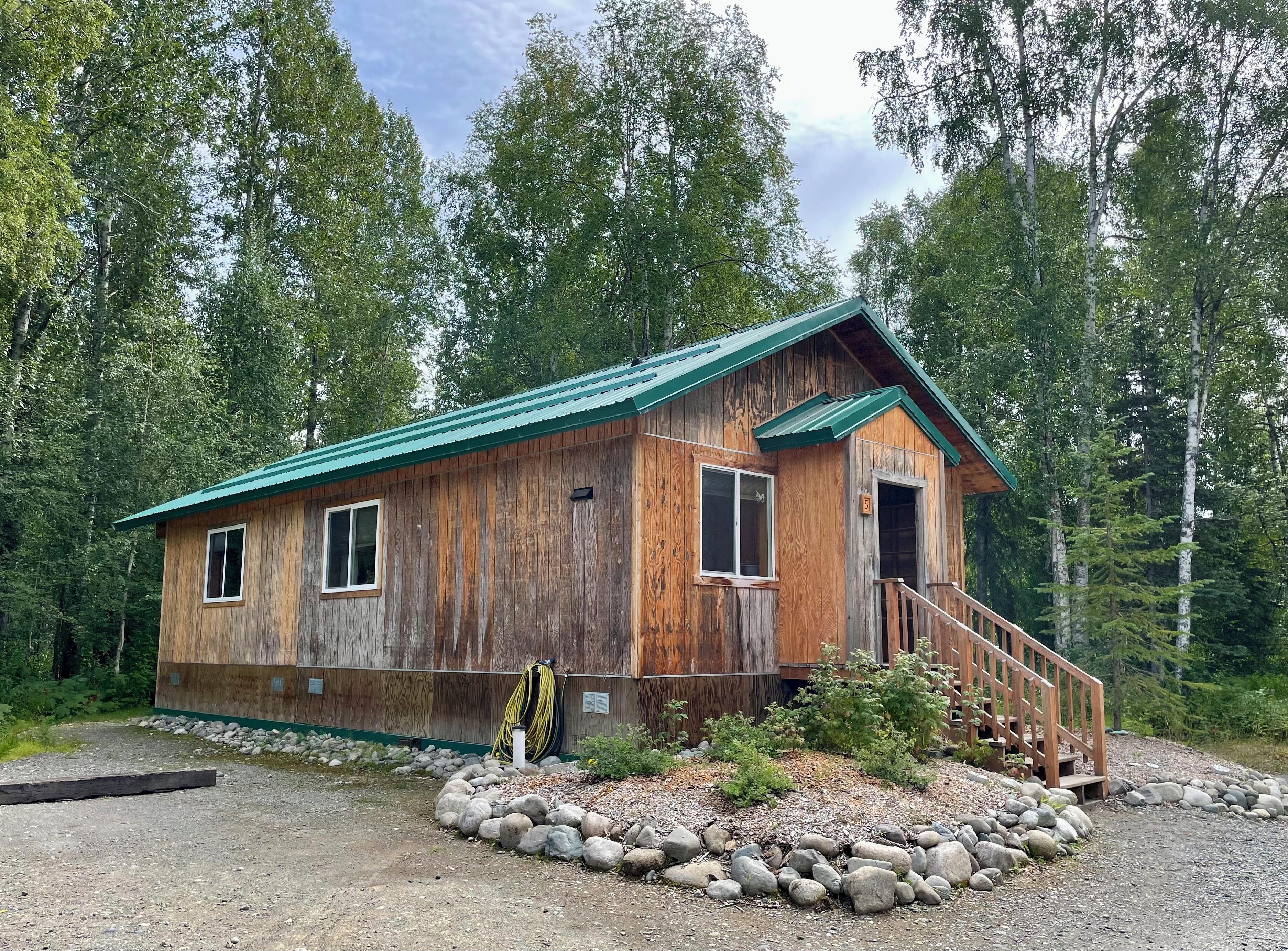 Une cabane en bois rustique, dotée d’un toit vert, d’une porte d’entrée et d’un petit porche avec des marches.