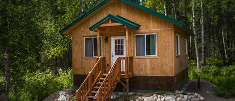 A wooden cabin with a green roof, a front door, and a staircase leading to the entrance.