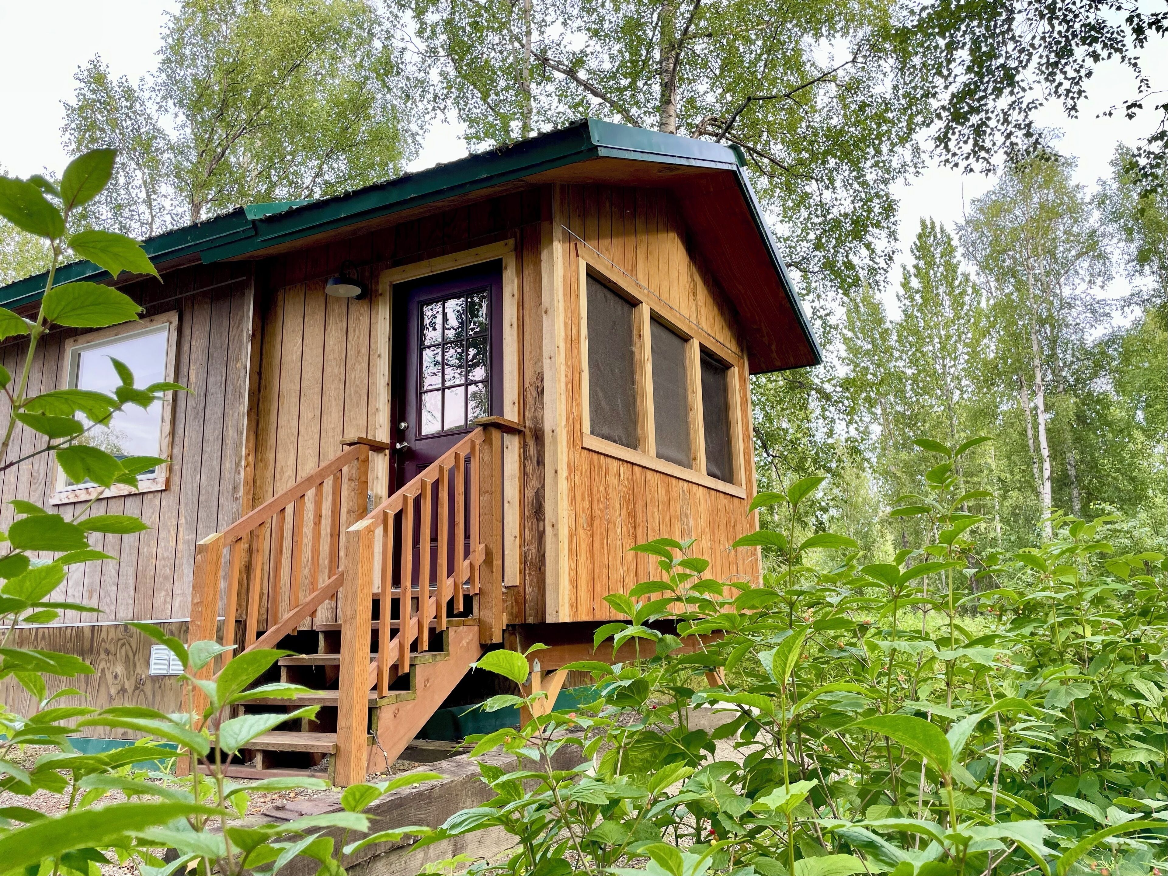 Une cabane en bois avec un escalier menant à une porte, le tout entouré de verdure.