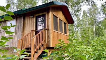 Une cabane en bois avec un escalier menant à une porte, le tout entouré de verdure.