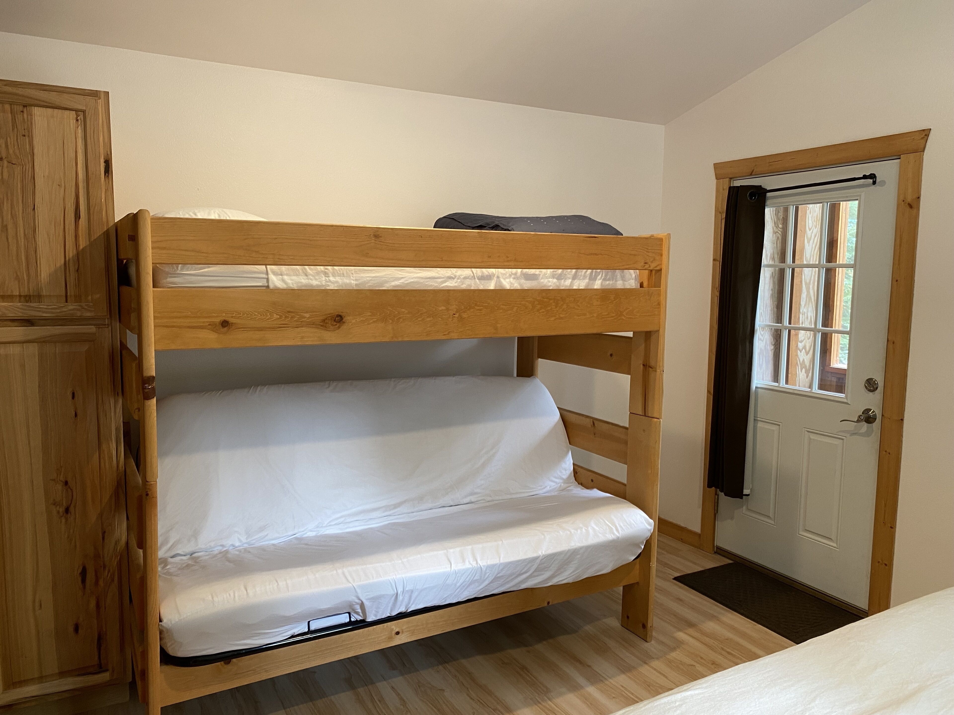 A bunk bed with a wooden frame, white bedding, and a door with a window.