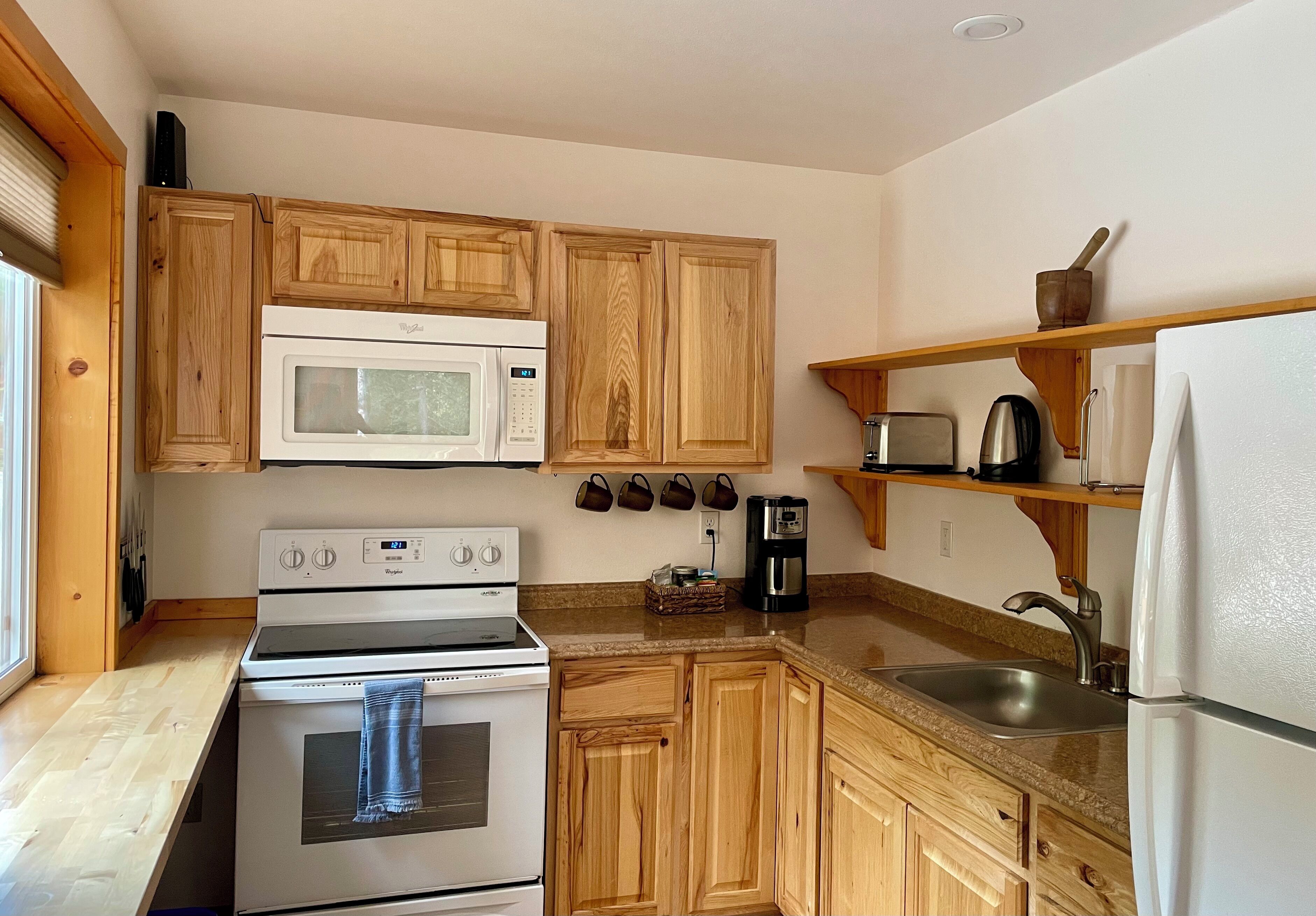 Una cocina con armarios de madera, un microondas, una estufa, un fregadero y un refrigerador.