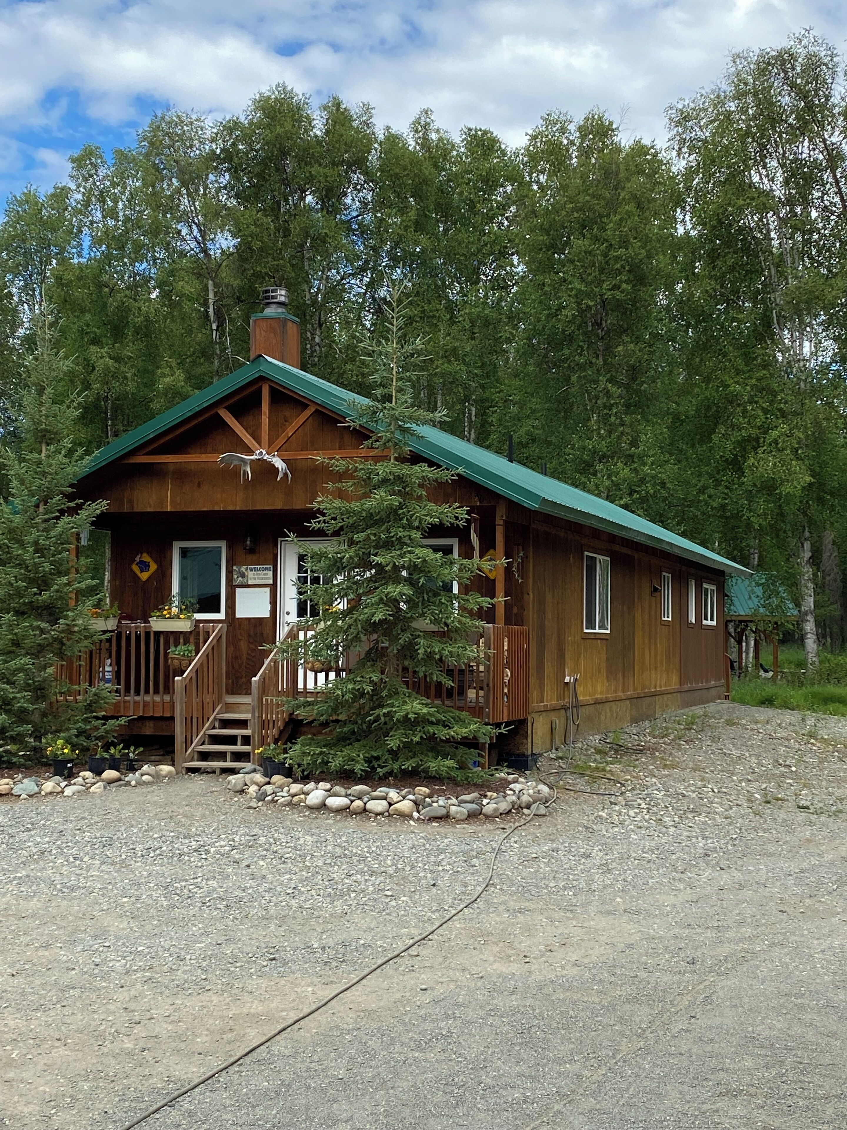 A wooden cabin with a green roof, a front porch, and a staircase leading to the entrance.