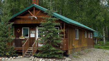 A wooden cabin with a green roof, a front porch, and a staircase leading to the entrance.