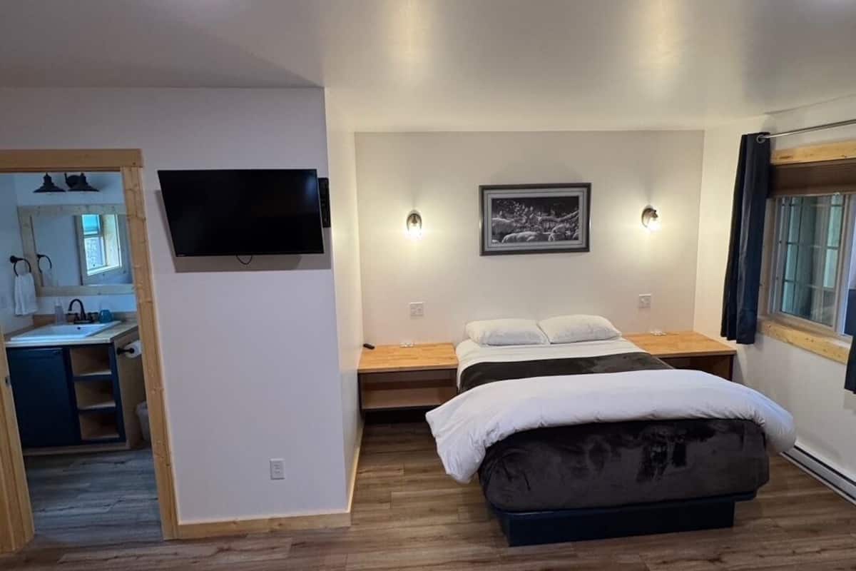 A bedroom with a bed, a TV mounted on the wall, and a window with curtains.