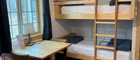 Ein kleines Zimmer mit Etagenbett, einem Holztisch mit Stuhl und einem Fenster mit Vorhängen.