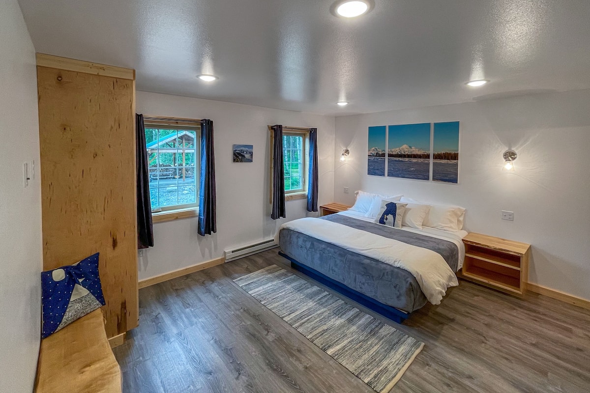 A bedroom with a bed, two windows, a wooden door, and a wall-mounted light fixture.