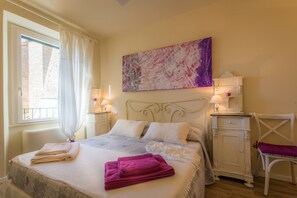 A bedroom with a bed, two bedside tables, a chair, a window with curtains, and a painting on the wall. - Viterbo Antica (Viterbo)