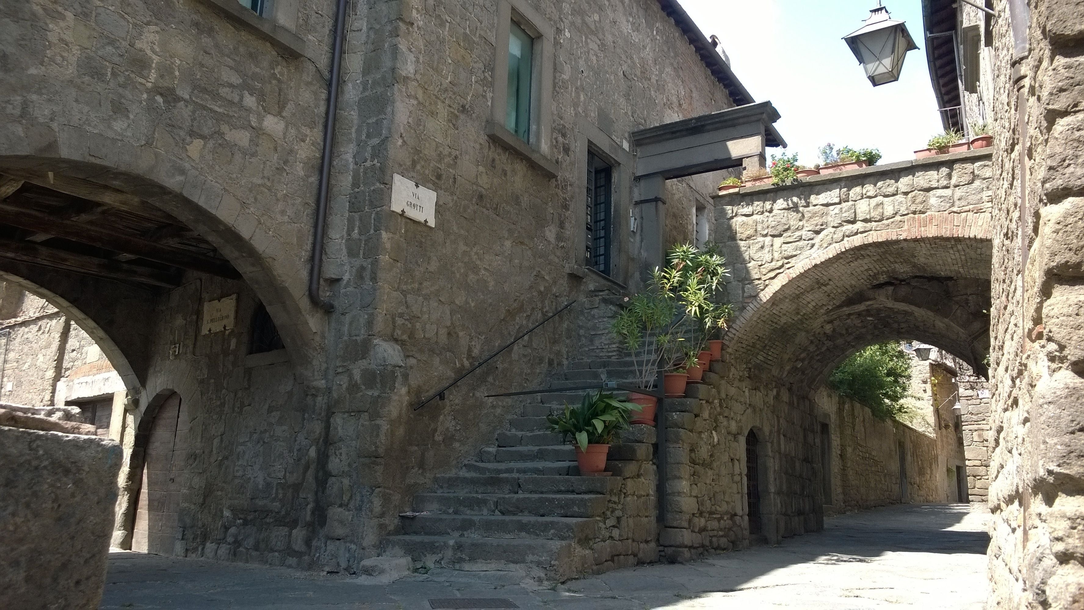 A narrow stone street with arched doorways and a staircase leading to a second level.