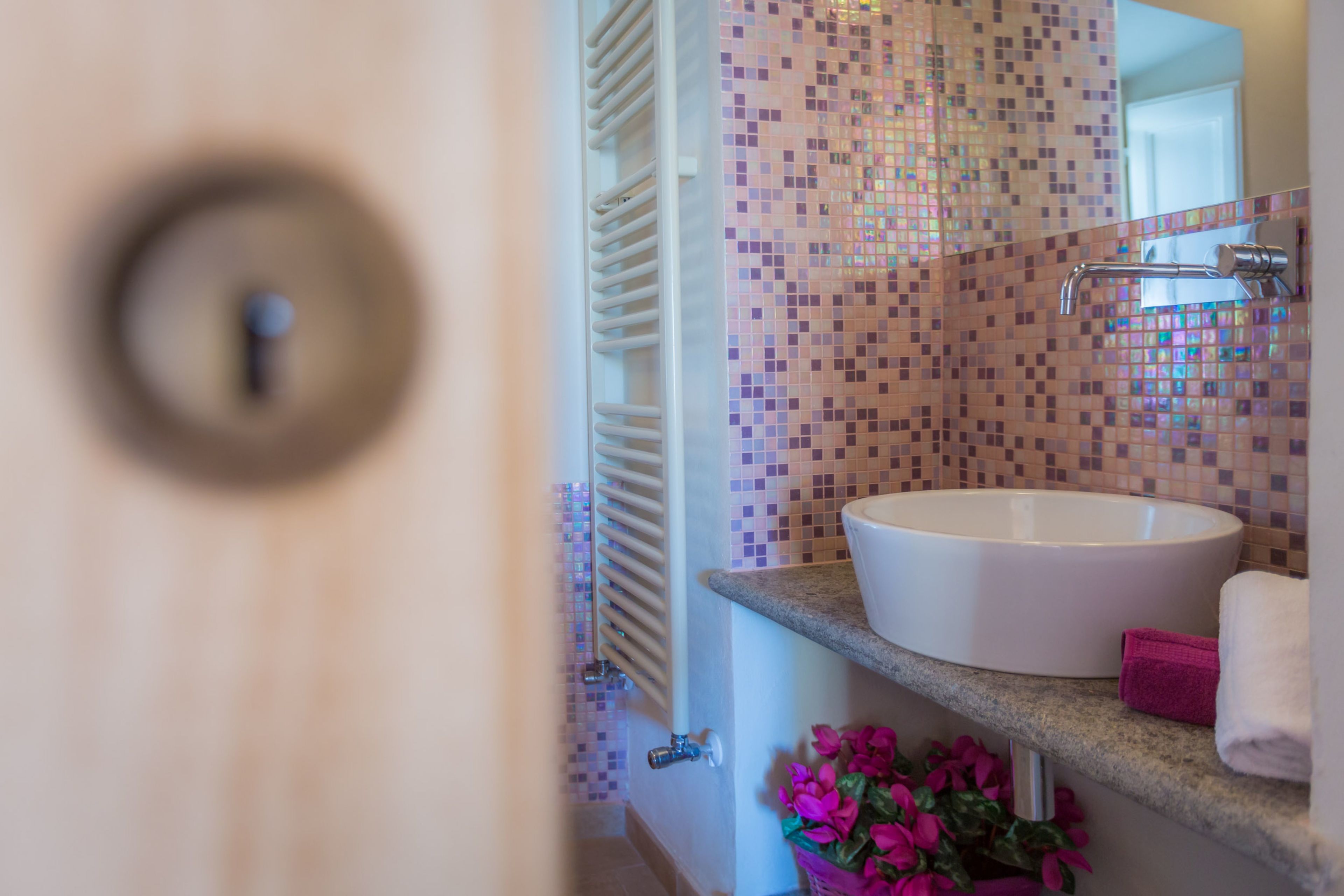 A bathroom with a tiled mosaic backsplash, a white sink, a towel rack, and a door with a round handle.