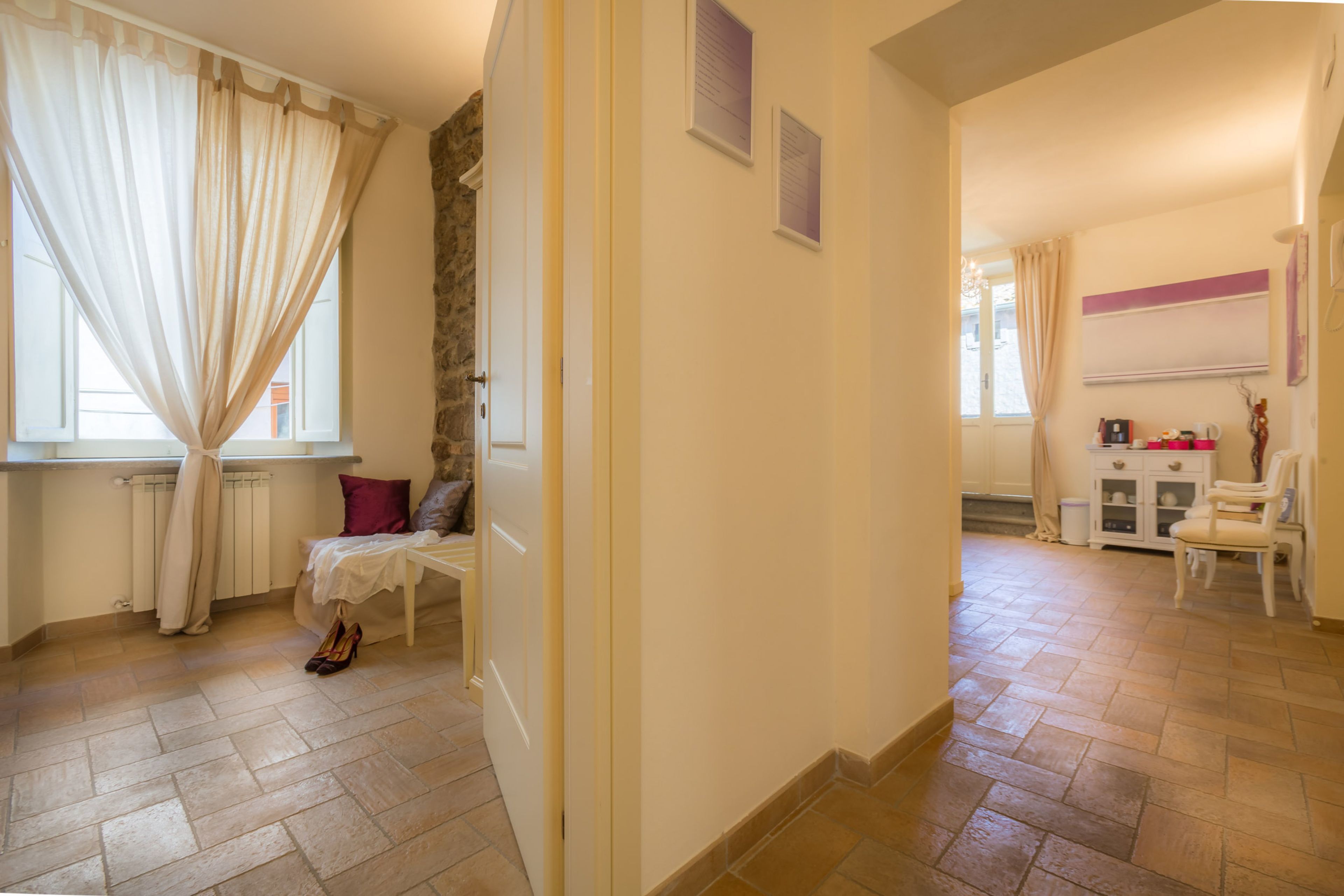 A room with a bed, a small table, a chair, a radiator, and a window with curtains.
