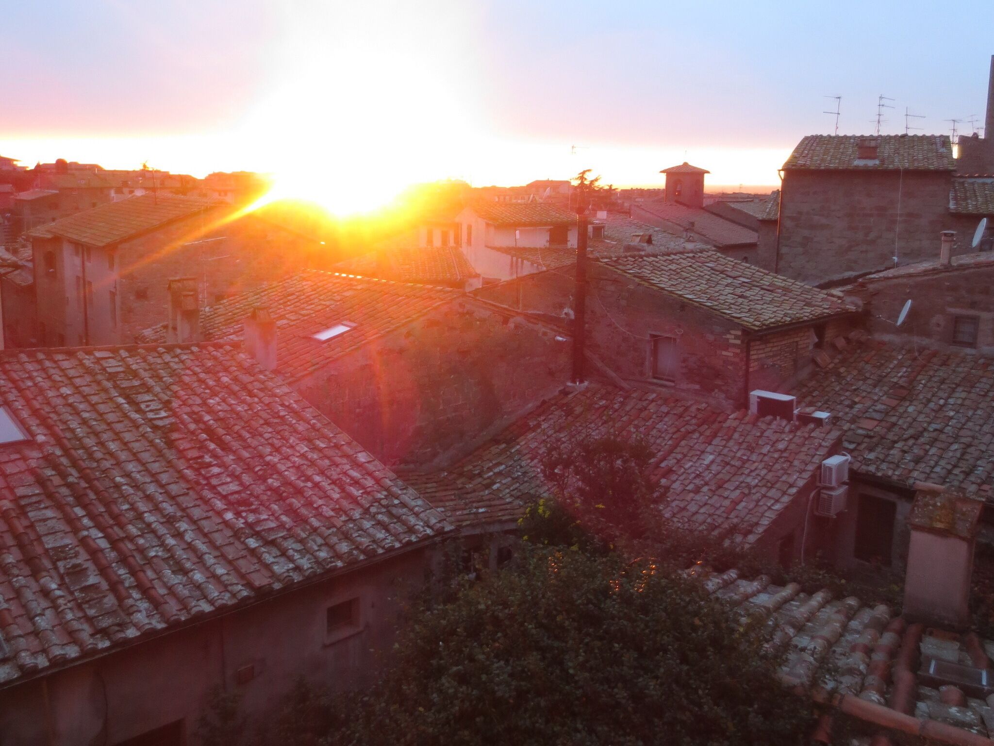 Blick auf eine Stadt mit traditionellen Gebäuden und einem Sonnenuntergang im Hintergrund.