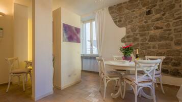 Un comedor con pared de piedra, muebles blancos y una mesa con una botella y flores.