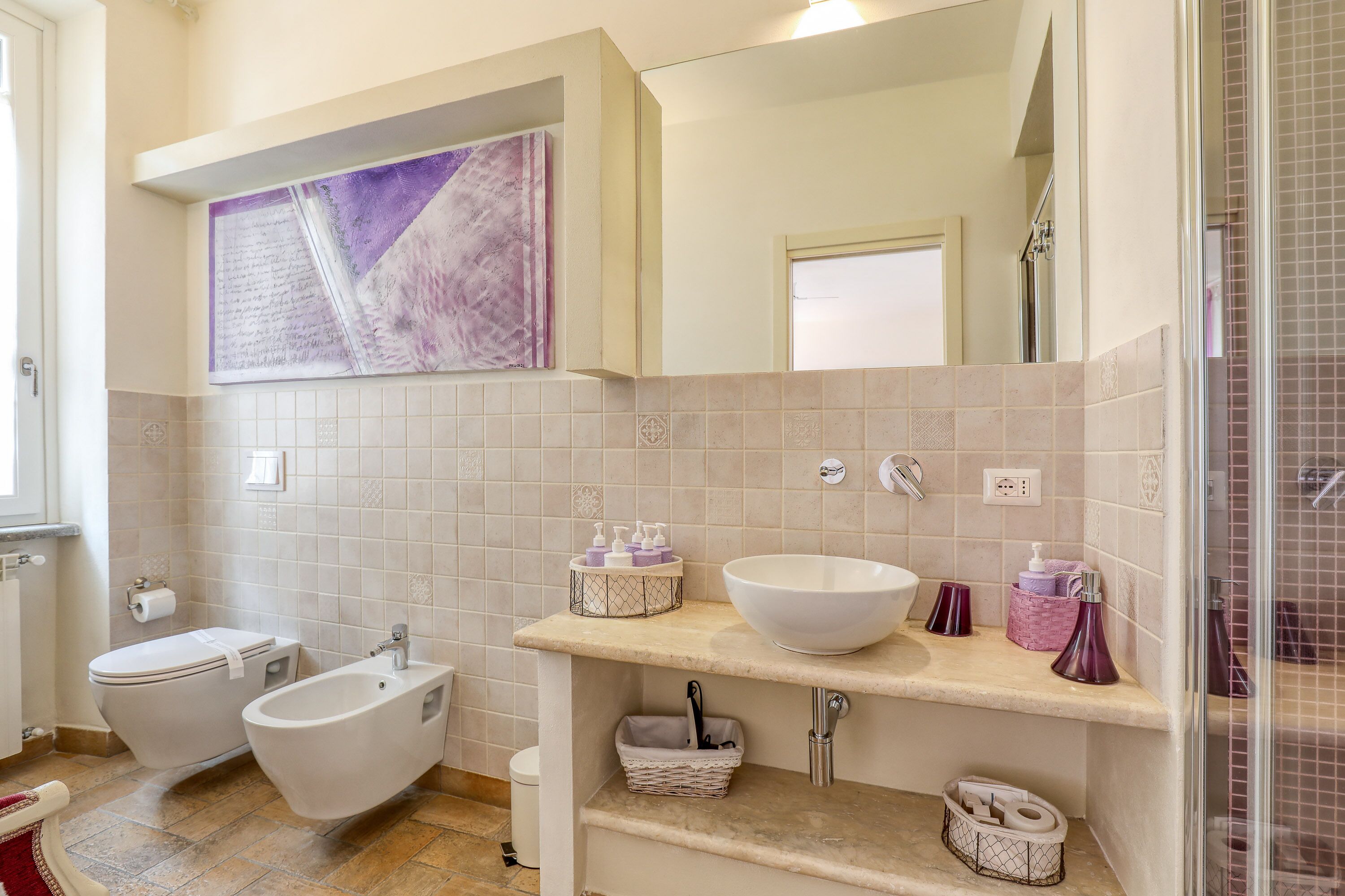 A modern bathroom with a bidet, toilet, and sink. There is a large mirror above the sink and a decorative wall piece.