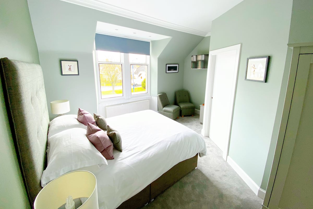A bedroom with a large bed, two chairs, a radiator, and a window with a view of the outside.